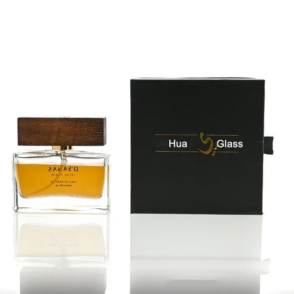 HUA0036 perfume bottle, heavy-base wide rectangular cuboid glass bottle with clear finish, featuring a side-set paper label, a metallic gold collar neck accent, and a prominent wide rectangular block-shaped wood cap with prominent natural wood grain lines, elegant modern fragrance packaging design available in 30ml, 50ml, and 100ml