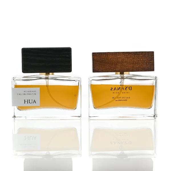 HUA0036 perfume bottle, heavy-base wide rectangular cuboid glass bottle with clear finish, featuring a side-set paper label, a metallic gold collar neck accent, and a prominent wide rectangular block-shaped wood cap with prominent natural wood grain lines, elegant modern fragrance packaging design available in 30ml, 50ml, and 100ml