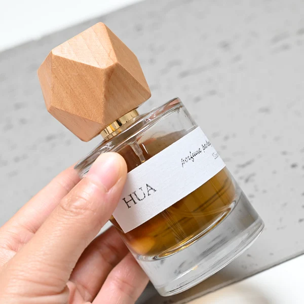 HUA0053 perfume bottle, heavy-base cylindrical round glass bottle with clear finish, featuring a wide wrapped paper label, a gold collar neck accent, and a unique polyhedral faceted diamond-shaped wood cap with subtle grain textures, elegant modern fragrance packaging design available in 30ml, 50ml, and 100ml