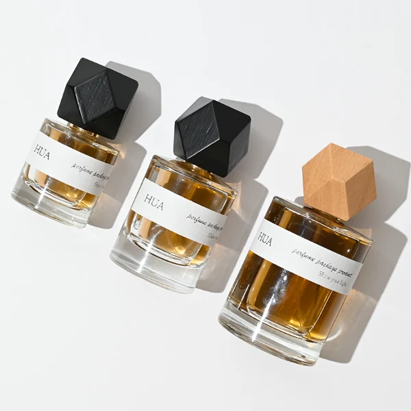 HUA0053 perfume bottle, heavy-base cylindrical round glass bottle with clear finish, featuring a wide wrapped paper label, a gold collar neck accent, and a unique polyhedral faceted diamond-shaped wood cap with subtle grain textures, elegant modern fragrance packaging design available in 30ml, 50ml, and 100ml