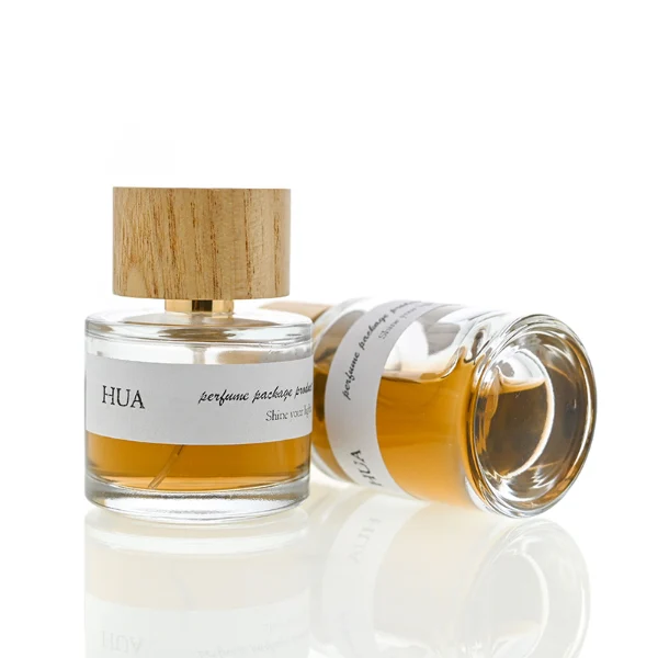 HUA0035 perfume bottle, heavy-base cylindrical round glass bottle with clear finish, featuring a horizontal paper label, a polished gold neck, and a wide cylindrical timber cap with a natural smooth grain finish, elegant modern fragrance packaging design available in 30ml, 50ml, and 100ml