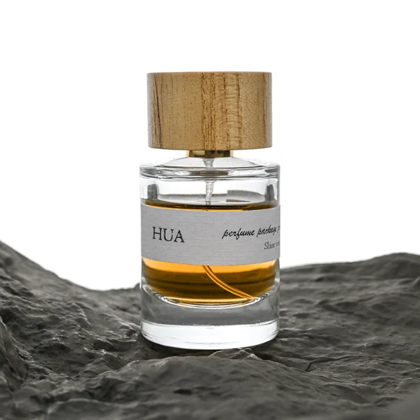 HUA0035 perfume bottle, heavy-base cylindrical round glass bottle with clear finish, featuring a horizontal paper label, a polished gold neck, and a wide cylindrical timber cap with a natural smooth grain finish, elegant modern fragrance packaging design available in 30ml, 50ml, and 100ml