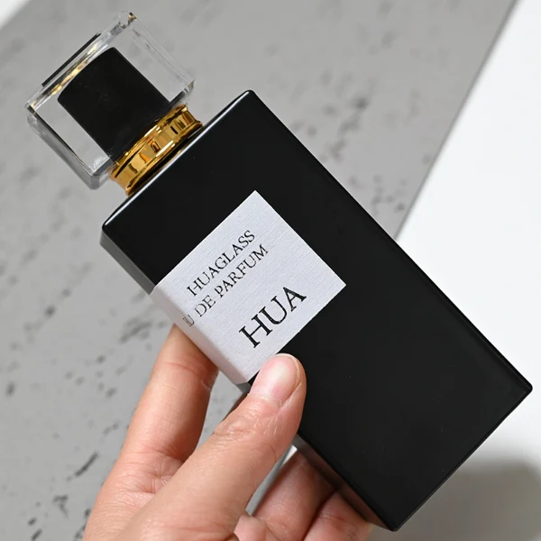 HUA0043 perfume bottle, heavy-base rectangular cuboid glass bottle with clear finish, featuring a side-aligned square paper label, a gold collar neck accent, and a unique double-layered square plastic cap with a transparent outer block and a colorful high-gloss shiny inner core, elegant modern fragrance packaging design available in 30ml, 50ml, and 100ml