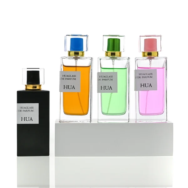 HUA0043 perfume bottle, heavy-base rectangular cuboid glass bottle with clear finish, featuring a side-aligned square paper label, a gold collar neck accent, and a unique double-layered square plastic cap with a transparent outer block and a colorful high-gloss shiny inner core, elegant modern fragrance packaging design available in 30ml, 50ml, and 100ml