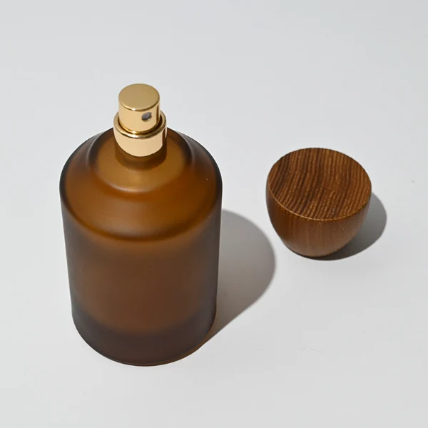 HUA0050 perfume bottle, cylindrical round glass bottle with multi-angled sloping beveled shoulders in solid high-gloss opaque black, clear amber, or frosted amber finish, featuring an eye-catching inverted conical cup-shaped wood cap with prominent natural wood grain lines, modern fragrance packaging design available in 30ml, 50ml, and 100ml