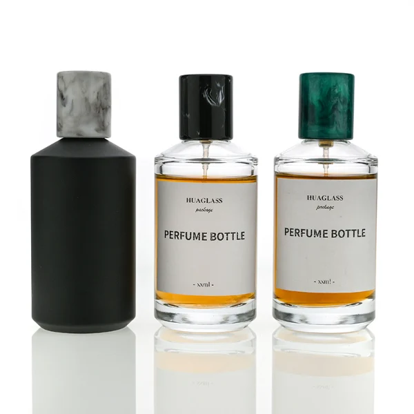 HUA0038 perfume bottle, heavy-base cylindrical round glass bottle with clear or solid high-gloss opaque black finish and unique chamfered sloping shoulders, featuring a tall cylindrical resin cap with an eye-catching marbled texture, elegant modern fragrance packaging design available in 30ml, 50ml, and 100ml