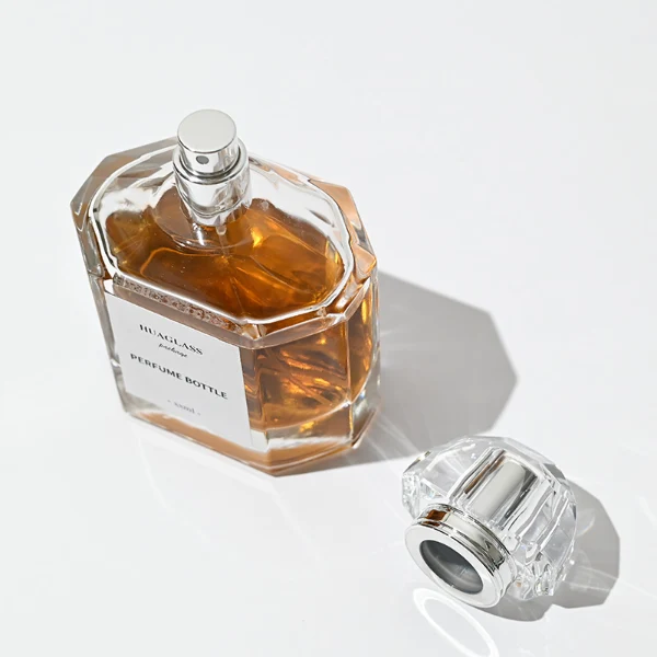 HUA0011 perfume bottle, luxury heavy-base polyhedral faceted glass bottle with high-transparency clear finish, featuring a square paper label and a brilliant multi-faceted crystalline acrylic plastic crown cap with a metallic inner core, elegant classic fragrance packaging design in 100ml