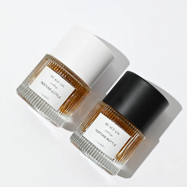 HUA0010 perfume bottle, heavy-base vertically ribbed cylindrical round glass bottle with clear finish, featuring a square paper label, a matching neck, and a tall cylindrical plastic cap with a smooth high-gloss shiny finish, elegant modern fragrance packaging design available in 40ml