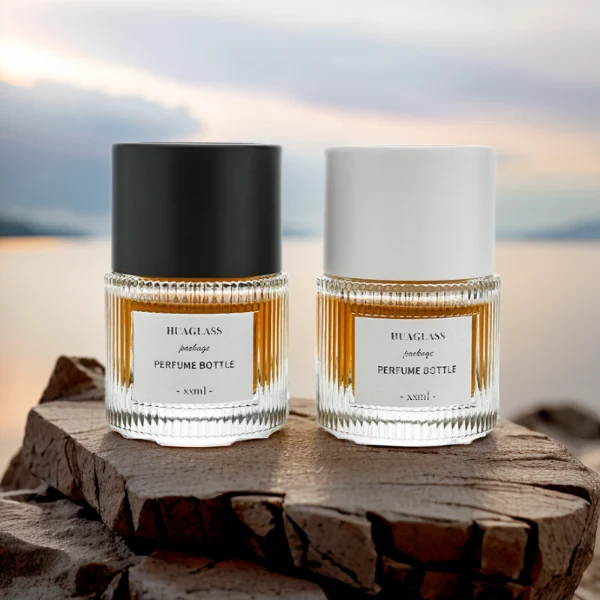 HUA0010 perfume bottle, heavy-base vertically ribbed cylindrical round glass bottle with clear finish, featuring a square paper label, a matching neck, and a tall cylindrical plastic cap with a smooth high-gloss shiny finish, elegant modern fragrance packaging design available in 40ml