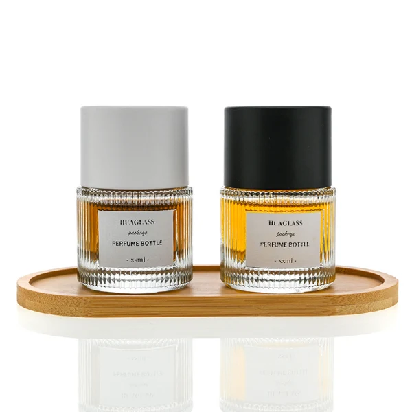 HUA0010 perfume bottle, heavy-base vertically ribbed cylindrical round glass bottle with clear finish, featuring a square paper label, a matching neck, and a tall cylindrical plastic cap with a smooth high-gloss shiny finish, elegant modern fragrance packaging design available in 40ml