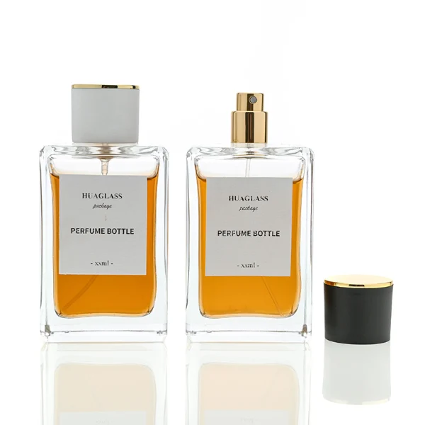 HUA0024 perfume bottle, heavy-base rectangular cuboid glass bottle with clear finish, featuring a large square paper label and a straight-sided cylindrical plastic cap with a smooth high-gloss finish and gold top trim, elegant modern fragrance packaging design in 100ml