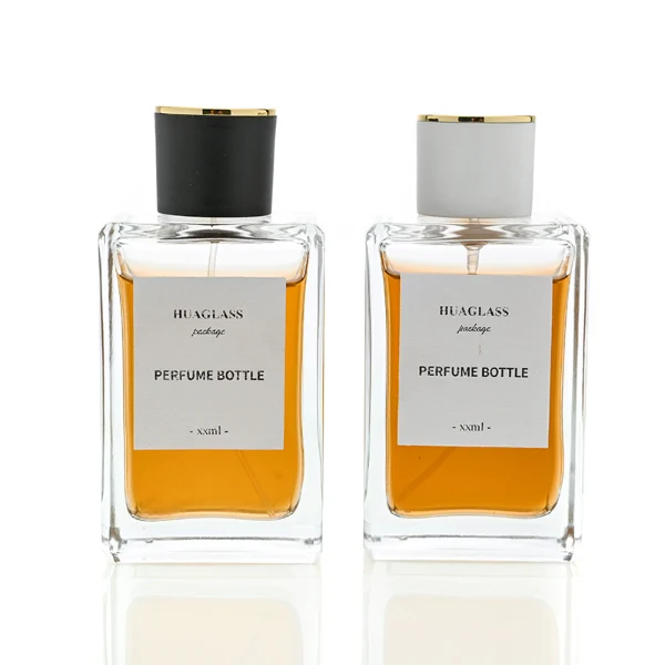 HUA0024 perfume bottle, heavy-base rectangular cuboid glass bottle with clear finish, featuring a large square paper label and a straight-sided cylindrical plastic cap with a smooth high-gloss finish and gold top trim, elegant modern fragrance packaging design in 100ml