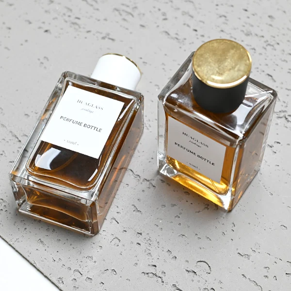 HUA0024 perfume bottle, heavy-base rectangular cuboid glass bottle with clear finish, featuring a large square paper label and a straight-sided cylindrical plastic cap with a smooth high-gloss finish and gold top trim, elegant modern fragrance packaging design in 100ml