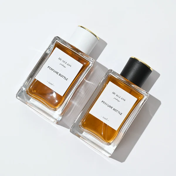 HUA0024 perfume bottle, heavy-base rectangular cuboid glass bottle with clear finish, featuring a large square paper label and a straight-sided cylindrical plastic cap with a smooth high-gloss finish and gold top trim, elegant modern fragrance packaging design in 100ml