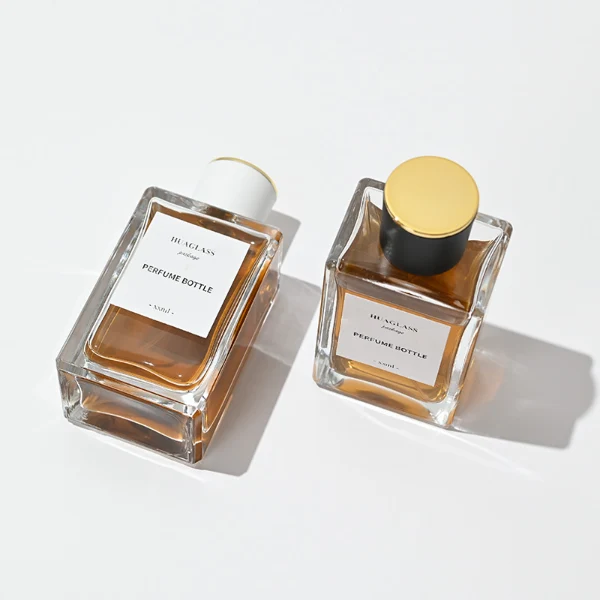 HUA0024 perfume bottle, heavy-base rectangular cuboid glass bottle with clear finish, featuring a large square paper label and a straight-sided cylindrical plastic cap with a smooth high-gloss finish and gold top trim, elegant modern fragrance packaging design in 100ml