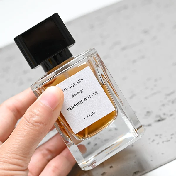 HUA0051 perfume bottle, heavy-base rectangular cuboid glass bottle with clear finish, featuring a square paper label, a black collar neck accent, and a short rectangular block-shaped solid black plastic cap with a smooth high-gloss shiny finish, elegant modern fragrance packaging design available in 30ml, 50ml, and 100ml
