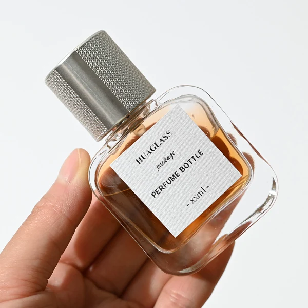 HUA0052 perfume bottle, heavy-base clear flattened oval flask glass bottle, featuring a square paper label and a tall cylindrical plastic cap with a smooth high-gloss shiny finish, elegant modern fragrance packaging design available in 30ml, 50ml, and 100ml