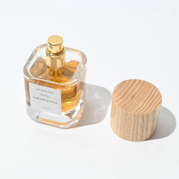 HUA0008 perfume bottle, luxury heavy-base cylindrical glass bottle with high-transparency clear finish, featuring a square paper label and a prominent tall flush-fit cylindrical natural textured wooden cap showcasing deep vertical wood grains, minimalist elegant fragrance packaging design available in 30ml, 50ml, and 100ml