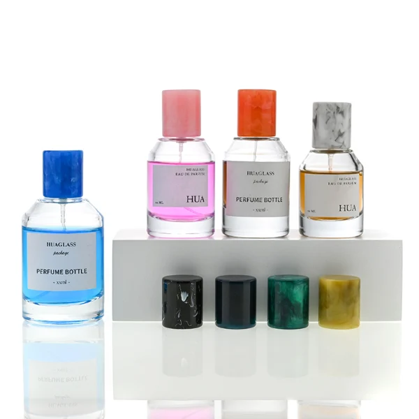 HUA0031 perfume bottle, heavy-base cylindrical glass bottle with a faceted shoulder and clear finish, featuring a square paper label, a matching neck, and a tall cylindrical resin cap with a colorful marbled finish, elegant modern fragrance packaging design available in 30ml, 50ml, and 100ml