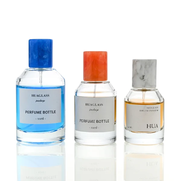 HUA0031 perfume bottle, heavy-base cylindrical glass bottle with a faceted shoulder and clear finish, featuring a square paper label, a matching neck, and a tall cylindrical resin cap with a colorful marbled finish, elegant modern fragrance packaging design available in 30ml, 50ml, and 100ml