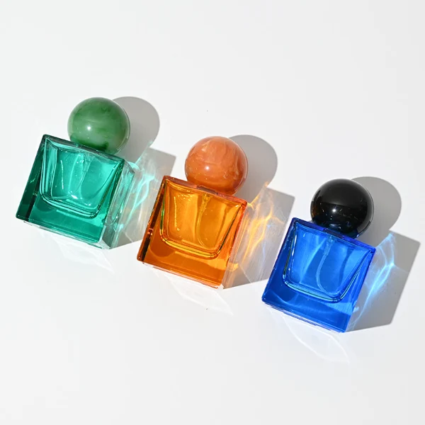 HUA0009 perfume bottle, luxury heavy-base square cuboid glass bottle with translucent deep multi-color finish, featuring a prominent oversized spherical solid colored resin cap showcasing opaque organic swirling veining and high-gloss textures, contemporary elegant fragrance packaging design available in 30ml, 50ml, and 100ml