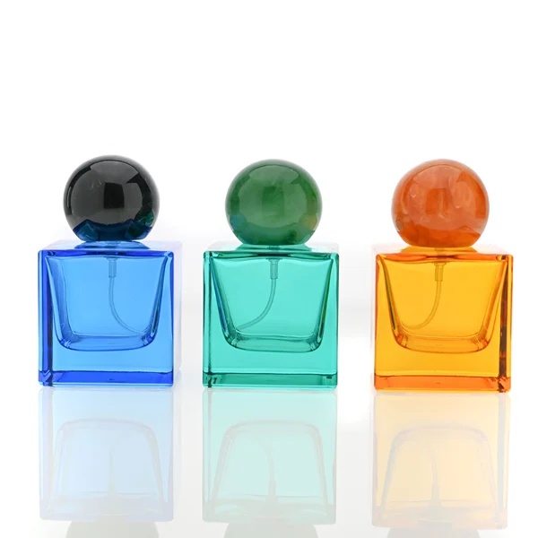 HUA0009 perfume bottle, luxury heavy-base square cuboid glass bottle with translucent deep multi-color finish, featuring a prominent oversized spherical solid colored resin cap showcasing opaque organic swirling veining and high-gloss textures, contemporary elegant fragrance packaging design available in 30ml, 50ml, and 100ml