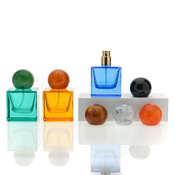 HUA0009 perfume bottle, luxury heavy-base square cuboid glass bottle with translucent deep multi-color finish, featuring a prominent oversized spherical solid colored resin cap showcasing opaque organic swirling veining and high-gloss textures, contemporary elegant fragrance packaging design available in 30ml, 50ml, and 100ml