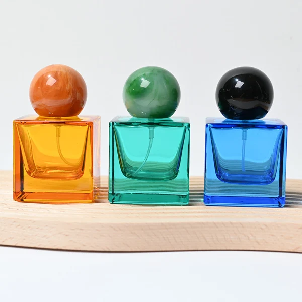 HUA0009 perfume bottle, luxury heavy-base square cuboid glass bottle with translucent deep multi-color finish, featuring a prominent oversized spherical solid colored resin cap showcasing opaque organic swirling veining and high-gloss textures, contemporary elegant fragrance packaging design available in 30ml, 50ml, and 100ml
