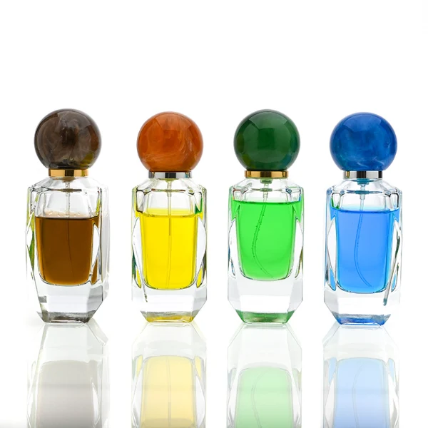 HUA0034 perfume bottle, heavy-base cylindrical glass bottle with a faceted shoulder and clear finish, featuring a square paper label, a polished gold or silver neck, and a tall cylindrical resin cap with a colorful marbled finish, elegant modern fragrance packaging design available in 50ml