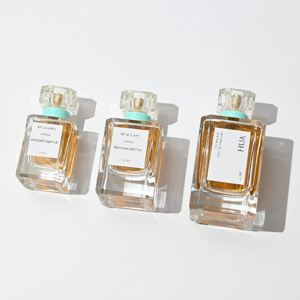 Vintage-inspired clear square plastic caps with a light mint green neck accent ring. Elegant square perfume bottles crafted from heavy-base clear glass filled with golden-amber liquid.