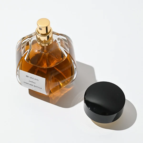 HUA0012 perfume bottle, heavy-base ribbed spherical round glass bottle with clear finish, featuring a square paper label, a matching neck, and a wide cylindrical plastic cap with a smooth high-gloss shiny black finish, elegant modern fragrance packaging design available in 100ml