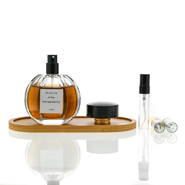 HUA0012 perfume bottle, heavy-base ribbed spherical round glass bottle with clear finish, featuring a square paper label, a matching neck, and a wide cylindrical plastic cap with a smooth high-gloss shiny black finish, elegant modern fragrance packaging design available in 100ml