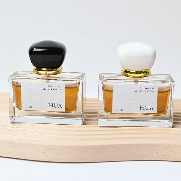 HUA0015 perfume bottle, heavy-base wide rectangular glass bottle with clear finish, featuring a square paper label, a polished gold neck, and a cushion-shaped plastic cap with a smooth high-gloss shiny finish, elegant modern fragrance packaging design available in 30ml, 50ml, and 100ml