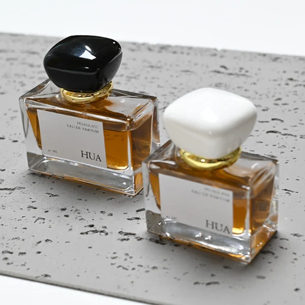 HUA0015 perfume bottle, heavy-base wide rectangular glass bottle with clear finish, featuring a square paper label, a polished gold neck, and a cushion-shaped plastic cap with a smooth high-gloss shiny finish, elegant modern fragrance packaging design available in 30ml, 50ml, and 100ml