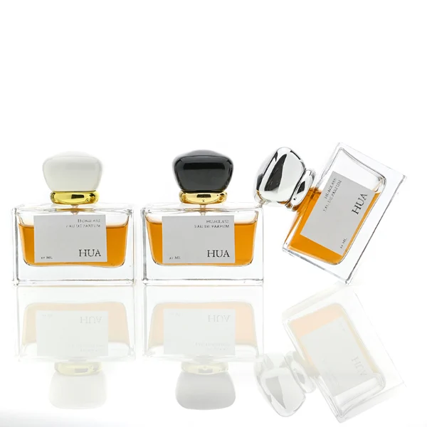 HUA0015 perfume bottle, heavy-base wide rectangular glass bottle with clear finish, featuring a square paper label, a polished gold neck, and a cushion-shaped plastic cap with a smooth high-gloss shiny finish, elegant modern fragrance packaging design available in 30ml, 50ml, and 100ml