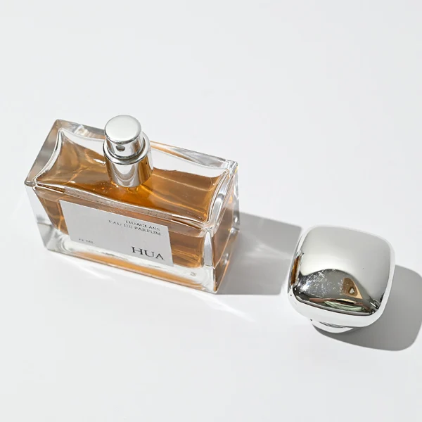 HUA0015 perfume bottle, heavy-base wide rectangular glass bottle with clear finish, featuring a square paper label, a polished gold neck, and a cushion-shaped plastic cap with a smooth high-gloss shiny finish, elegant modern fragrance packaging design available in 30ml, 50ml, and 100ml