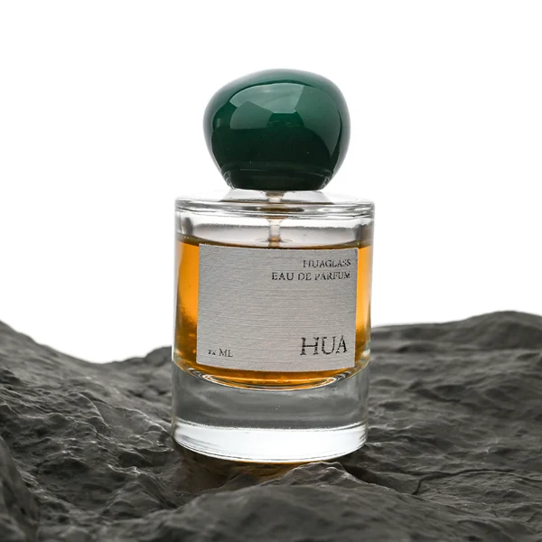 HUA0026 perfume bottle, heavy-base cylindrical round glass bottle with clear finish, featuring a square paper label and an organic smooth pebble-shaped plastic cap with a high-gloss shiny finish, elegant modern fragrance packaging design available in 30ml, 50ml, and 100ml