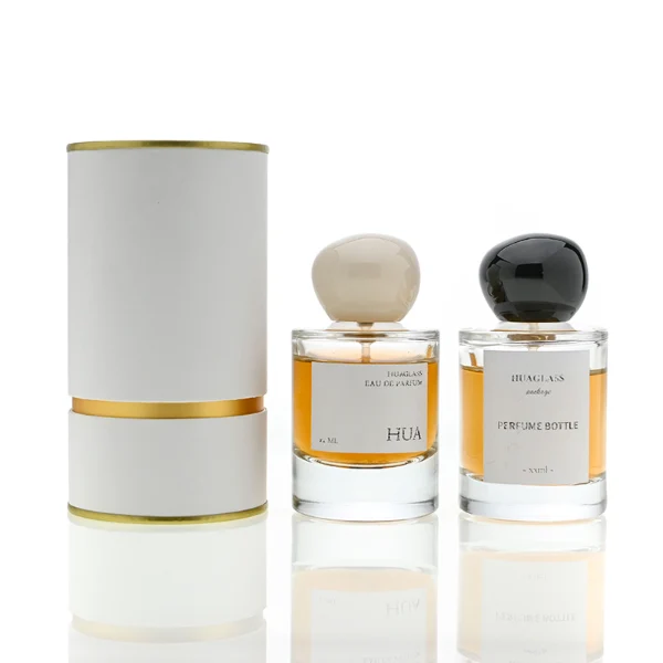 HUA0026 perfume bottle, heavy-base cylindrical round glass bottle with clear finish, featuring a square paper label and an organic smooth pebble-shaped plastic cap with a high-gloss shiny finish, elegant modern fragrance packaging design available in 30ml, 50ml, and 100ml
