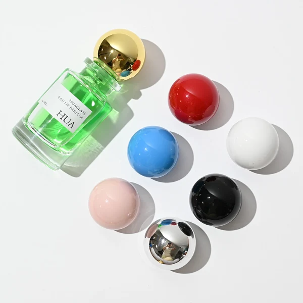 HUA0062 perfume bottle, heavy-base cylindrical round glass bottle with clear finish, featuring a square paper label, a matching neck with ribbon bow decorations, and a playful spherical ball-shaped plastic cap with a smooth high-gloss shiny finish, elegant modern fragrance packaging design available in 30ml, 50ml, and 100ml
