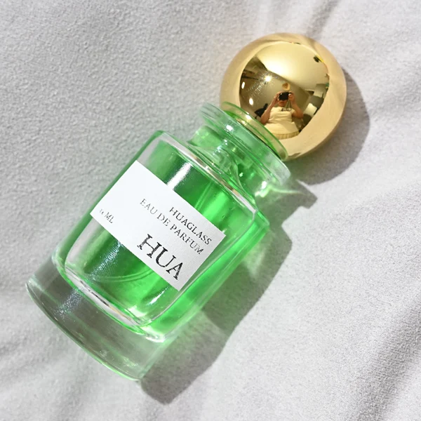 HUA0062 perfume bottle, heavy-base cylindrical round glass bottle with clear finish, featuring a square paper label, a matching neck with ribbon bow decorations, and a playful spherical ball-shaped plastic cap with a smooth high-gloss shiny finish, elegant modern fragrance packaging design available in 30ml, 50ml, and 100ml