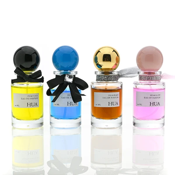 HUA0062 perfume bottle, heavy-base cylindrical round glass bottle with clear finish, featuring a square paper label, a matching neck with ribbon bow decorations, and a playful spherical ball-shaped plastic cap with a smooth high-gloss shiny finish, elegant modern fragrance packaging design available in 30ml, 50ml, and 100ml