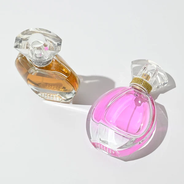 HUA0069 perfume bottles, oval clear glass with faceted plastic caps in silver/gold tones, amber and pink liquids, modern elegant design, 30ml 50ml 100ml.