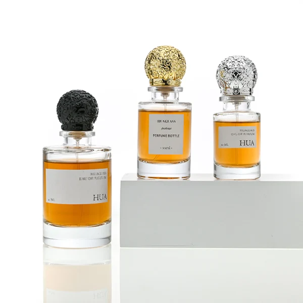 HUA0076 perfume bottle, cylindrical clear glass with liquid, ornate textured spherical cap in silver gold or black finish, modern elegant design, available in 35 ml, 50 ml, and 100 ml