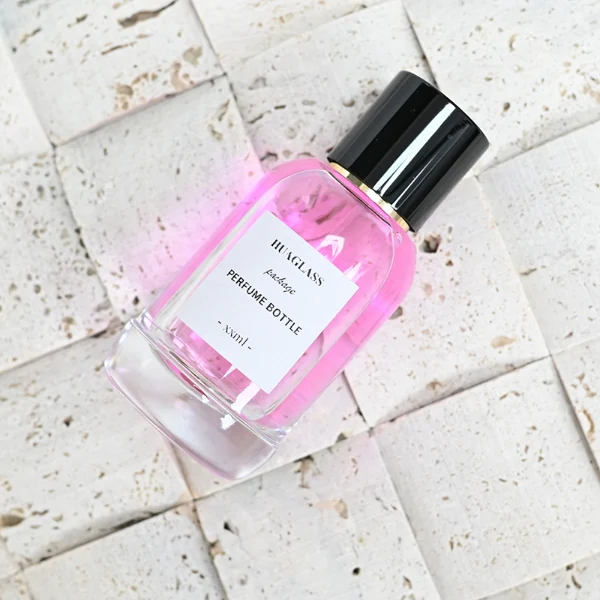 HUA0077 perfume bottle, rounded clear glass with liquid, glossy black aluminum magnetic cap, modern elegant design, available in 50 ml and 100 ml