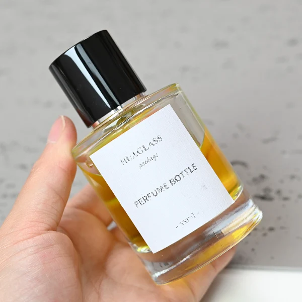 HUA0079 perfume bottle, cylindrical clear glass with liquid, glossy black aluminum magnetic cap, modern minimalist design, available in 30 ml, 50 ml, and 100 ml