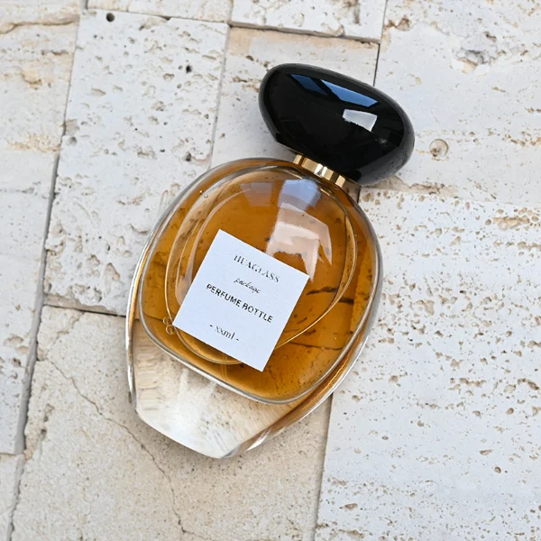 HUA0080 perfume bottle, oval internally sprayed glass with liquid, glossy black rounded plastic cap with irregular gold edge texture, modern elegant design, available in 30 ml, 50 ml, 75 ml, and 100 ml