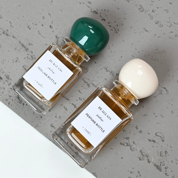 HUA0085 perfume bottle, rectangular clear glass body with liquid, irregular spherical plastic cap with glass neck, modern elegant design, available in 30 ml, 50 ml, and 100 ml.