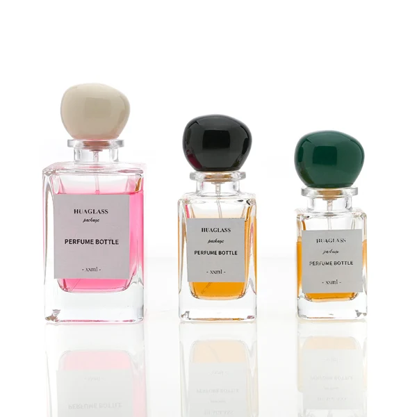 HUA0085 perfume bottle, rectangular clear glass body with liquid, irregular spherical plastic cap with glass neck, modern elegant design, available in 30 ml, 50 ml, and 100 ml.