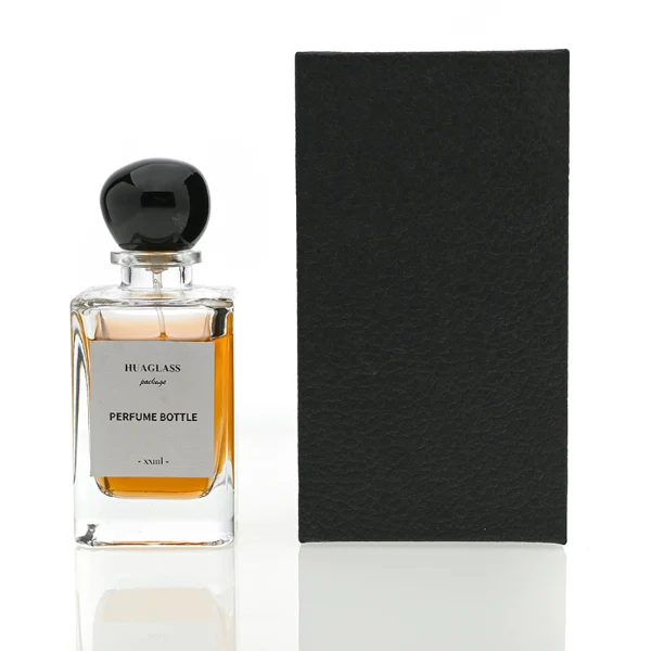 HUA0085 perfume bottle, rectangular clear glass body with liquid, irregular spherical plastic cap with glass neck, modern elegant design, available in 30 ml, 50 ml, and 100 ml.