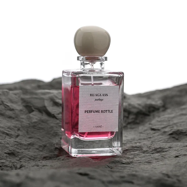 HUA0085 perfume bottle, rectangular clear glass body with liquid, irregular spherical plastic cap with glass neck, modern elegant design, available in 30 ml, 50 ml, and 100 ml.